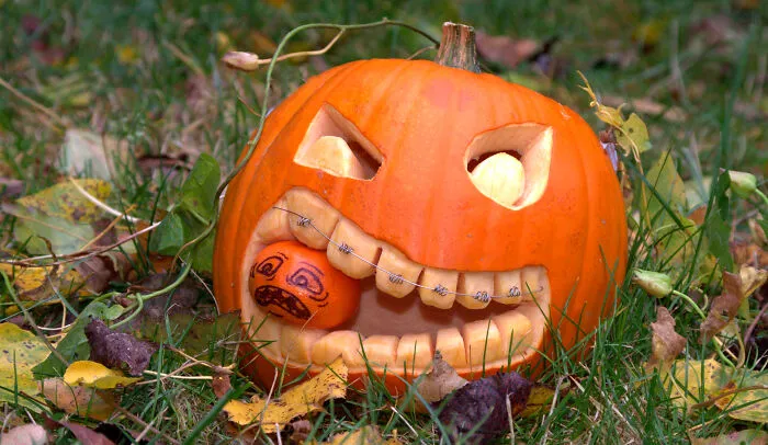 Carved Halloween pumpkin with a small decorated pumpkin in its mouth in a garden Halloween village for wild mice.