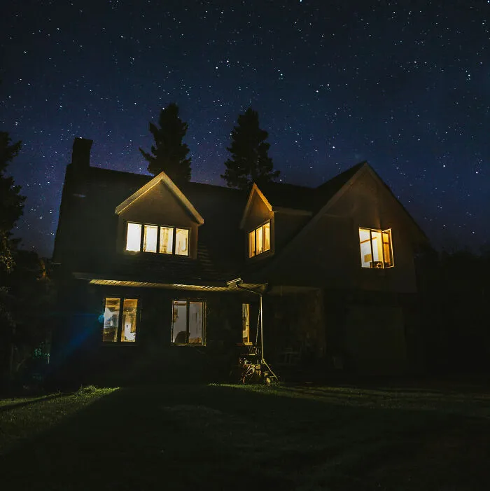 House lit up at night under a starry sky, illustrating a story about people living next to horrible neighbors.