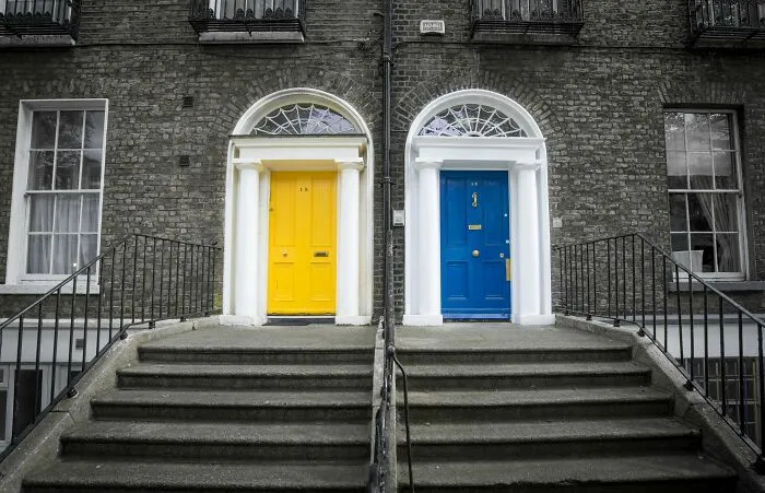 Two front doors, one yellow and one blue, with spider web decorations above, for a creepy Halloween-inspired would you rather poll.