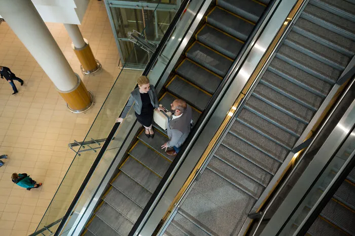 Two businesspeople talking on an escalator in a mall, illustrating 911 operators strange calls that were true cases.