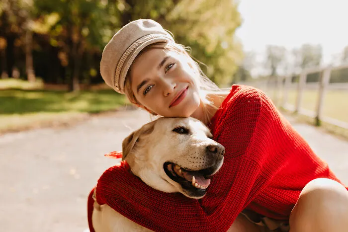 Woman wearing a hat and red sweater hugging her intelligent pet dog outdoors, showcasing surprising pet behavior.