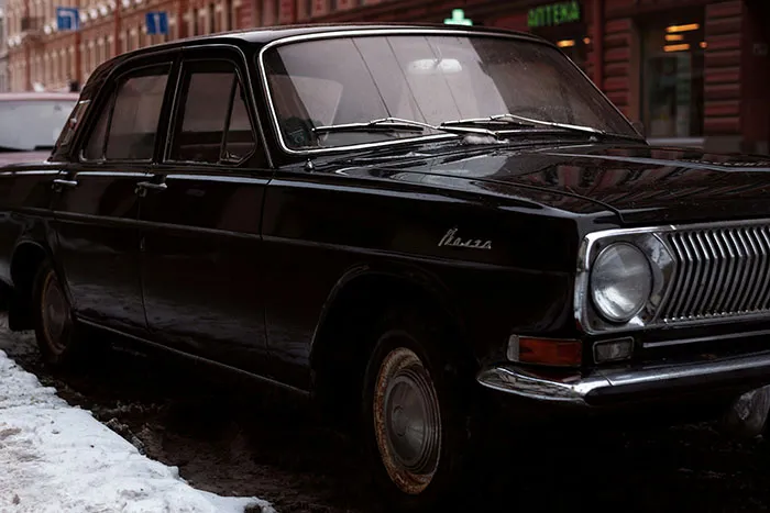 Vintage black car parked on a city street at dusk, evoking spooky urban legends in an eerie urban setting.