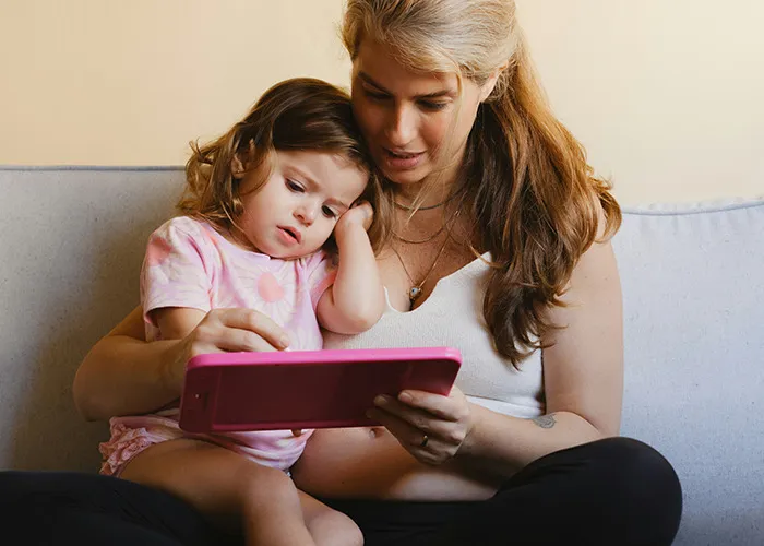 Mother and daughter sitting on couch together, using a tablet, illustrating the topic of benefits for women to get married.