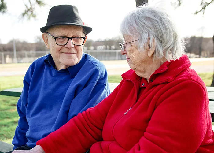 Elderly couple sitting on a bench outdoors, representing women discussing benefits of marriage and relationships.