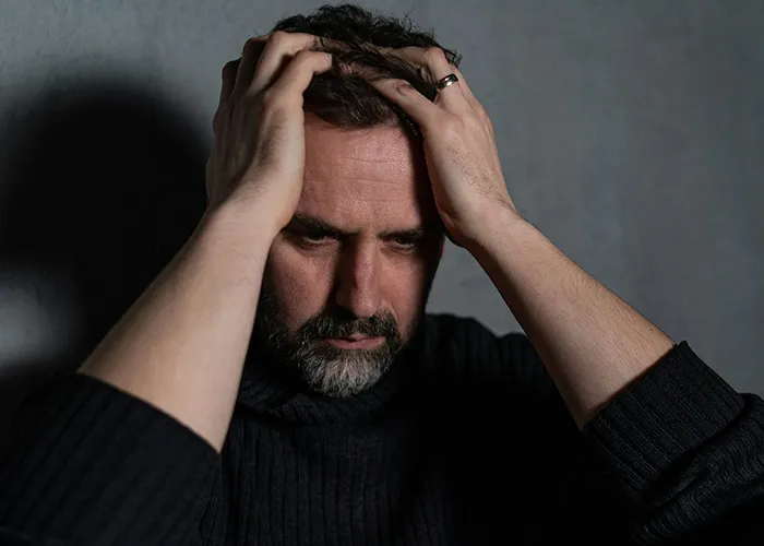 Man with beard holding his head in frustration, reflecting on benefits of marriage for women, in a dimly lit room.