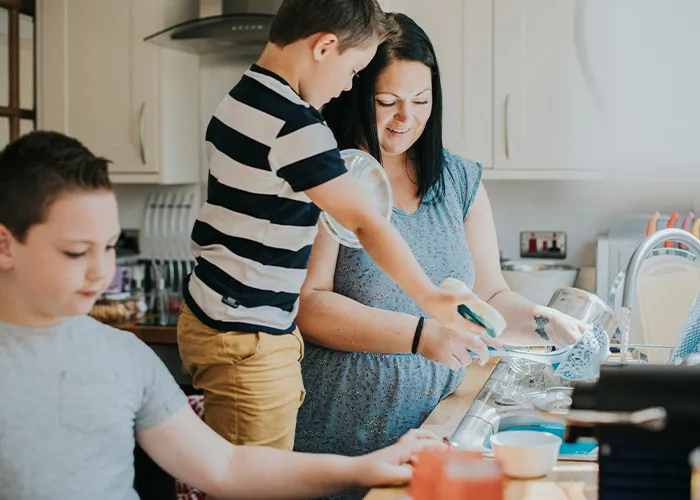 Woman and children washing dishes together in kitchen, illustrating the benefits of marriage for women and family life.