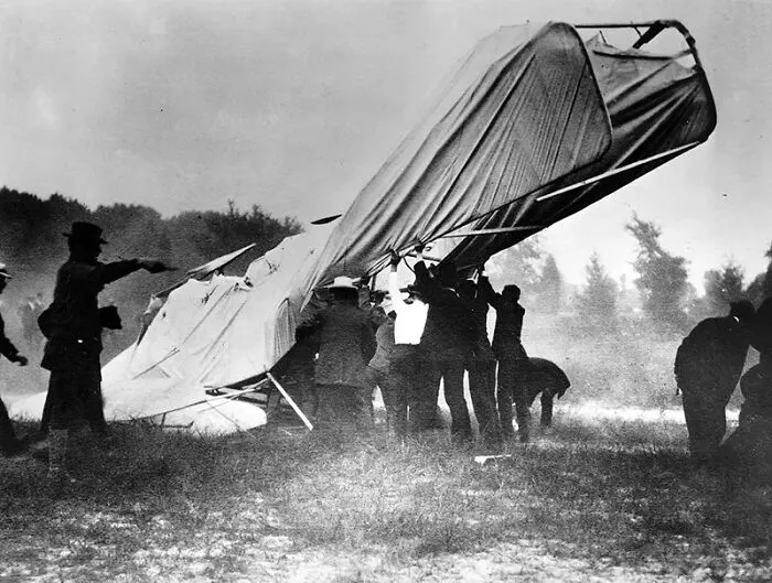 Early photography capturing a group of men handling a large fabric-covered glider outdoors in a grassy field.
