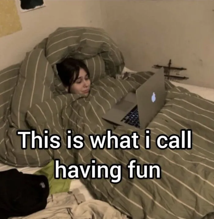 Person wrapped in striped blankets using a laptop in bed, relatable meme about coping with anxiety and having fun.