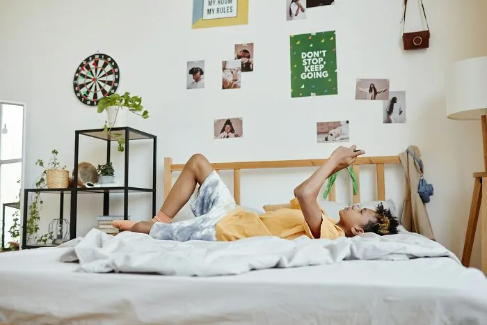 Person lying on bed in a bedroom decorated with photos and posters, contemplating shocking and dark secrets in life.