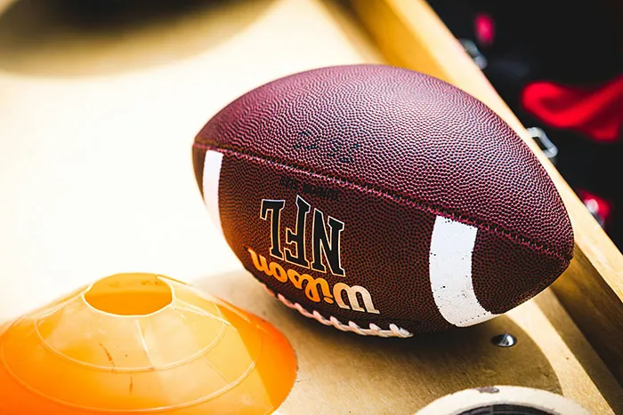 Close-up of an NFL Wilson football on a wooden surface next to an orange training cone used in sports practice.