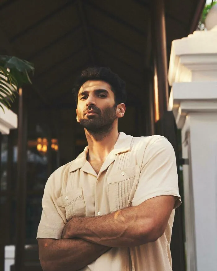 Aditya Roy Kapur posing confidently with arms crossed in casual beige shirt, representing the most handsome man in the world 2025.