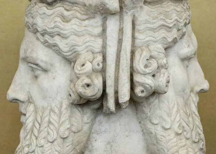 Ancient marble sculpture of a two-faced head with detailed curly hair and beards, symbolizing duality and contrast.