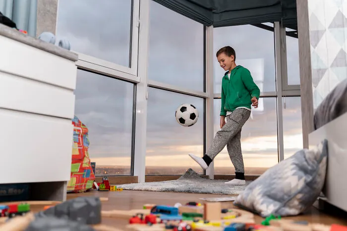 Young boy kicking a soccer ball indoors in a messy room, illustrating challenges of living next to horrible people.