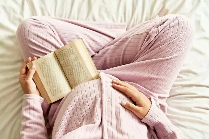 Person in pink ribbed loungewear reading a book while sitting cross-legged, reflecting on popular kids turned outcasts in school.