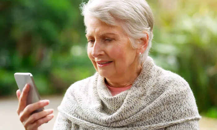Elderly woman outdoors smiling while looking at her smartphone, illustrating strange 911 operator calls that were true.