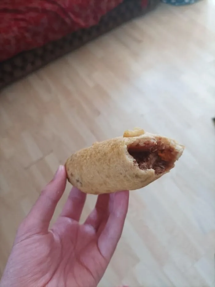 Hand holding a partially eaten pastry with filling, illustrating foods not popular in their country despite tourist expectations.