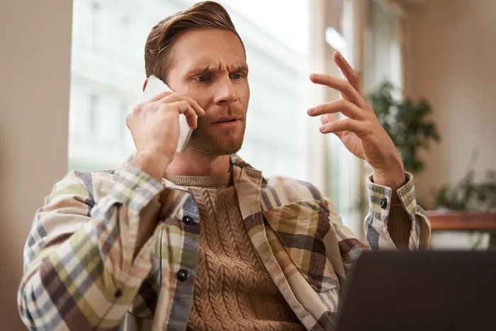 Man in a plaid shirt making a confused phone call, illustrating strange 911 operator calls that turned out to be true