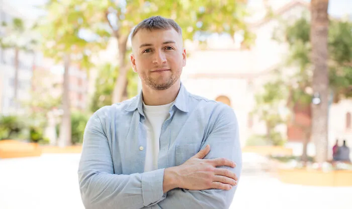 Young man standing outdoors with arms crossed, smiling confidently while highlighting loopholes to take advantage of.