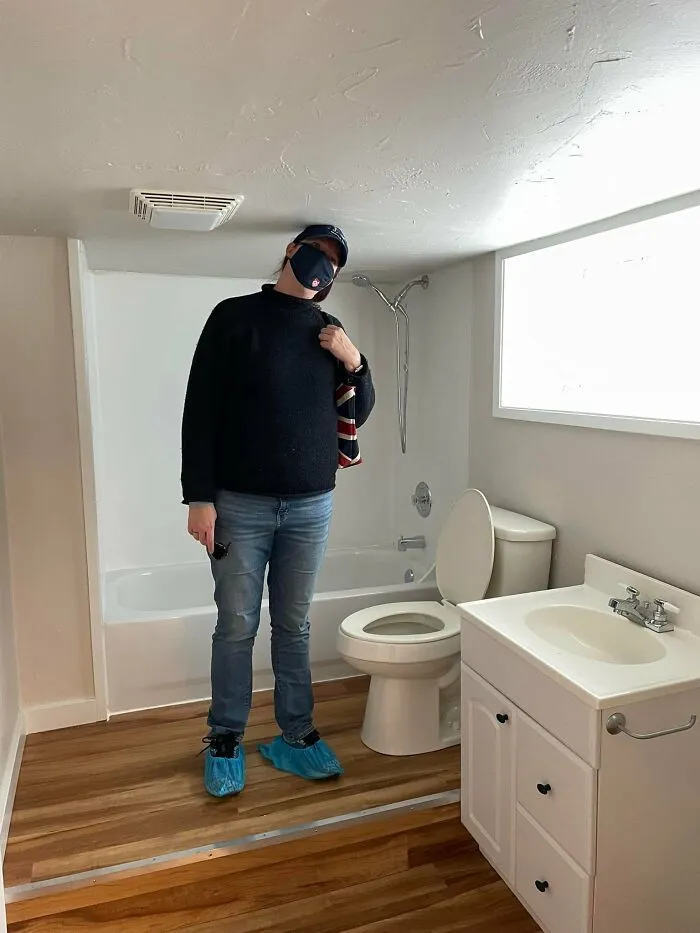 Persona con mascarilla y gorra en un baño pequeño con inodoro y lavabo, ejemplo de listados Zillow tan malos que parecen falsos.