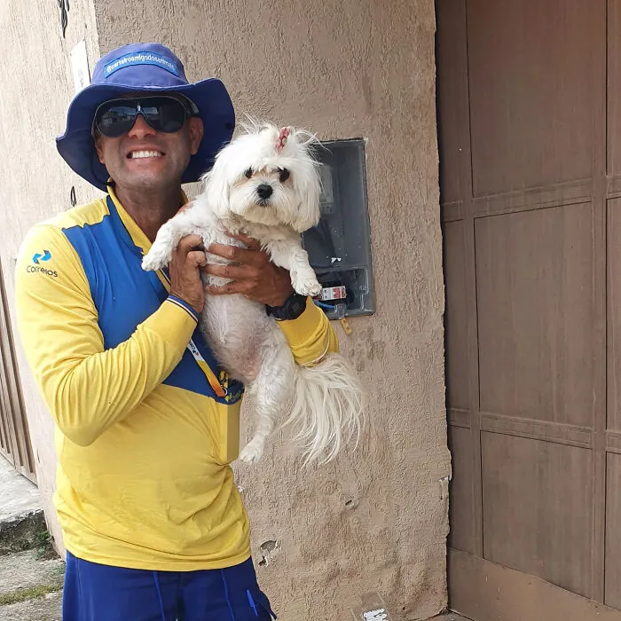 Mailman smiling and holding a small white dog, showing the bond between mailman and dogs on his route.