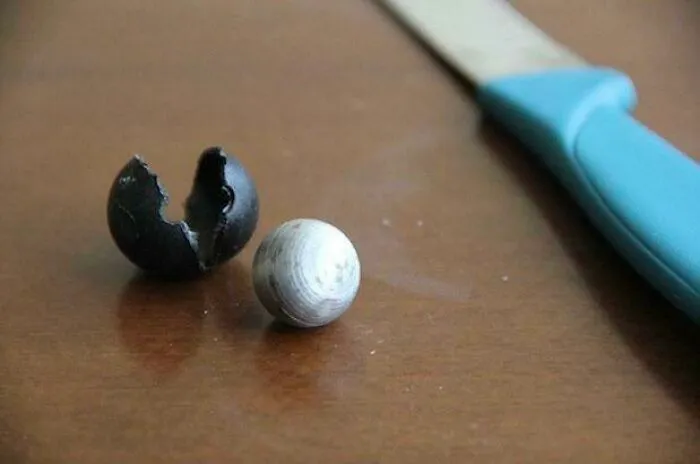 Cracked black olive revealing its white inside next to a knife on a wooden surface showing rare insides of things.