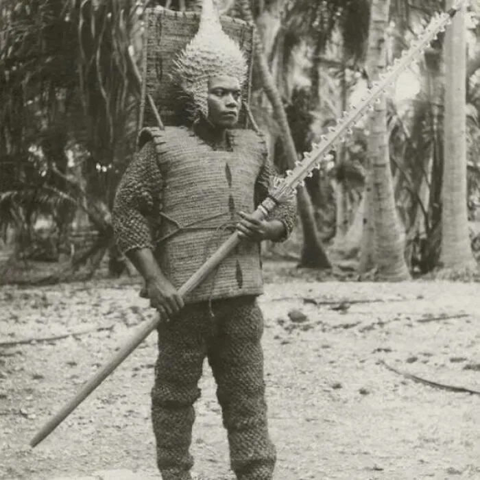 Un guerrero kiribatiano de Beru, ataviado con una armadura hecha de las resistentes fibras exteriores de la cáscara del coco, un casco de pez globo seco y empuñando una lanza de diente de tiburón.