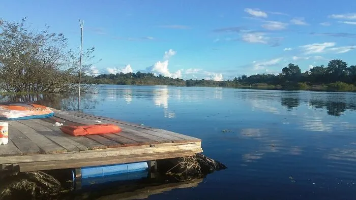 Peaceful remote location by a calm lake with a wooden dock and clear blue sky reflecting on the water.