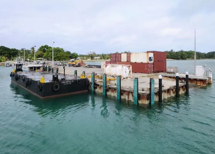 Remote dock with cargo containers and boats in clear water surrounded by greenery, showcasing mind-blowing remote locations.