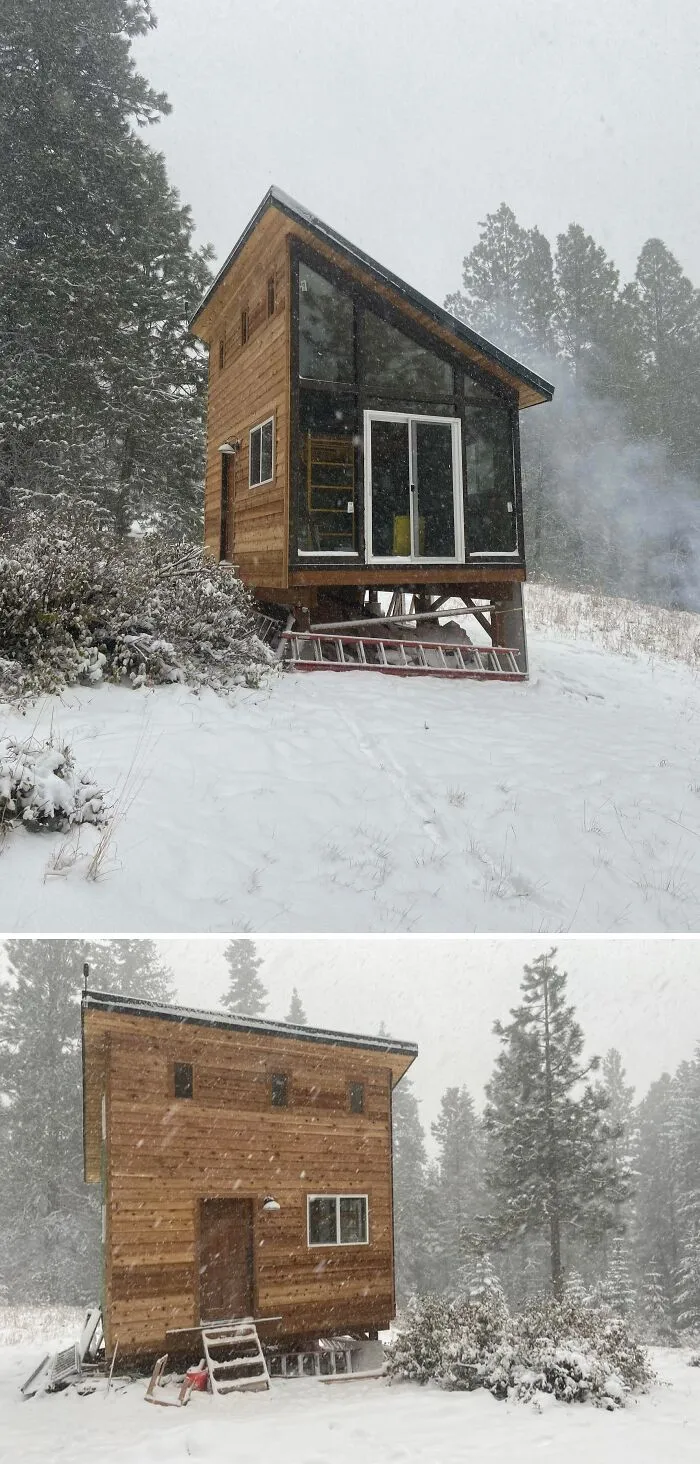Cozy off-grid cabin elevated in snowy forest setting with large windows, surrounded by pine trees during a winter snowfall.