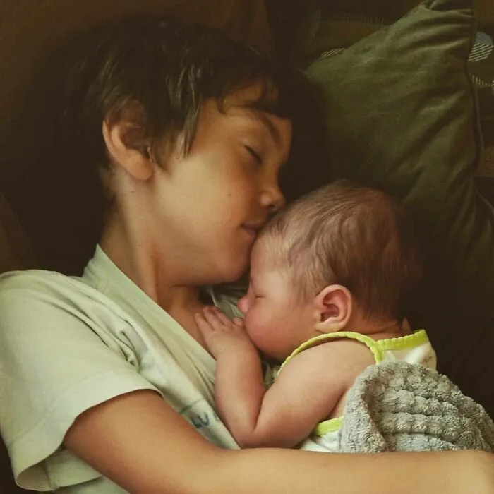 Young boy holding and cuddling a sleeping baby, capturing a heartwarming moment of dreams turned into reality.