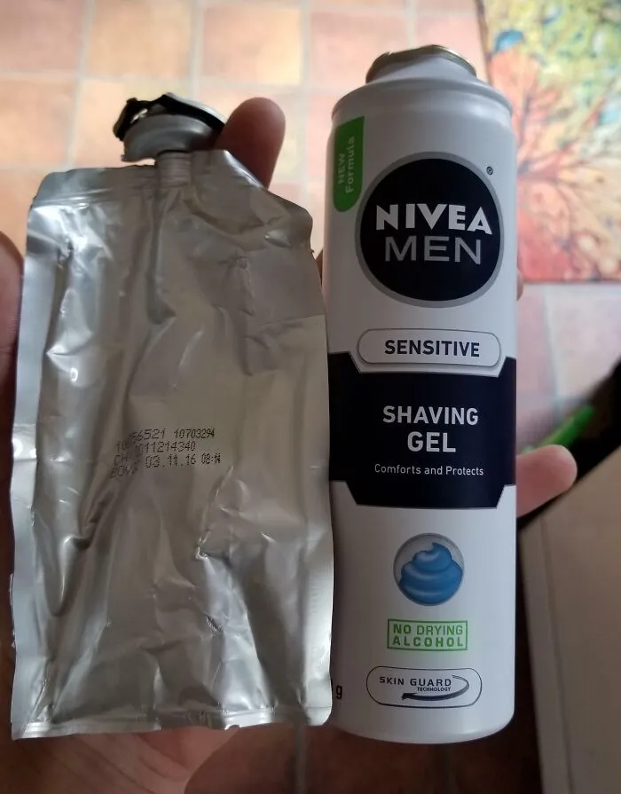 Hand holding a Nivea Men shaving gel can alongside its foil pouch showing the insides of packaging.