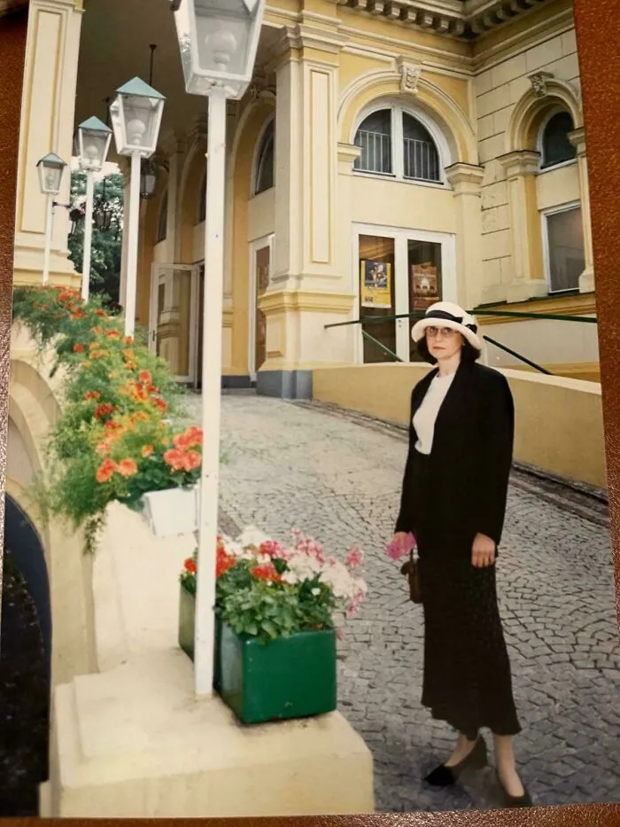 Woman in vintage outfit standing on cobblestone street near flowers and historic yellow building in a where was this taken post.