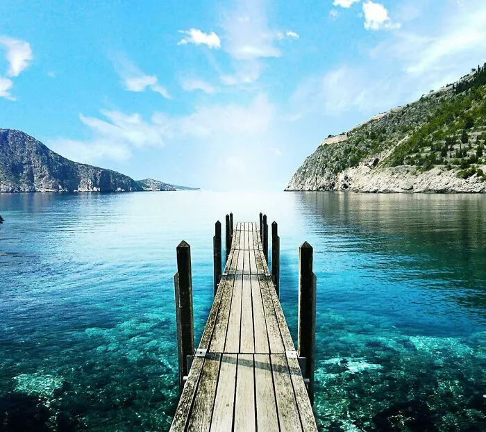 Wooden pier extending into clear blue water between rocky cliffs in a scenic location for where was this taken posts.