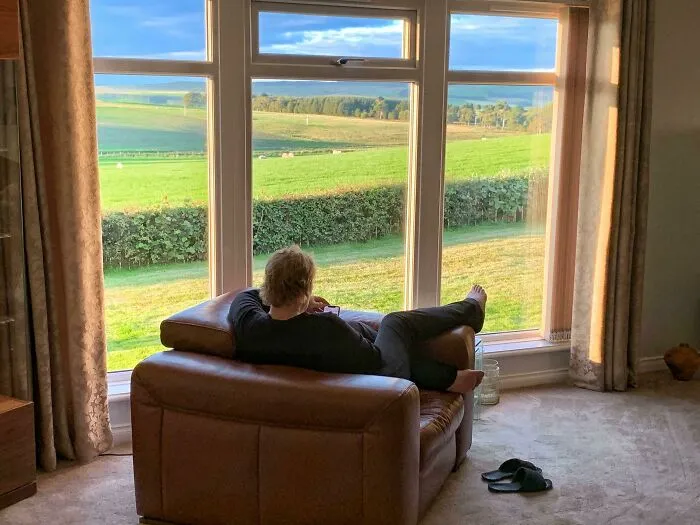 Person relaxing on a leather chair by a large window, enjoying a peaceful view that inspires dream fulfillment.
