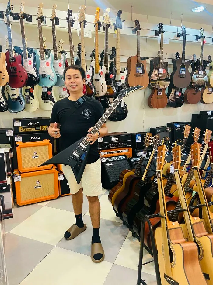 Man holding electric guitar in music store filled with guitars, representing people turning their dreams into reality.