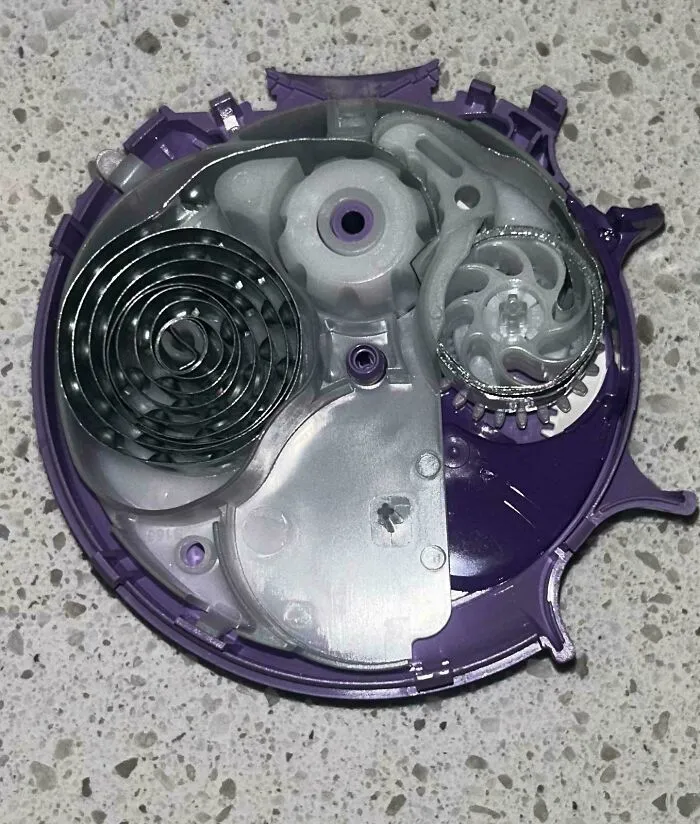 Close-up of the insides of a mechanical device showing coiled springs and gears on a speckled surface.