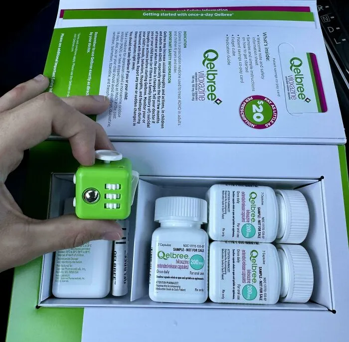 Mano sosteniendo un cubo antiestrés en un kit organizado de medicamentos Qelbree para soluciones ingeniosas diarias.