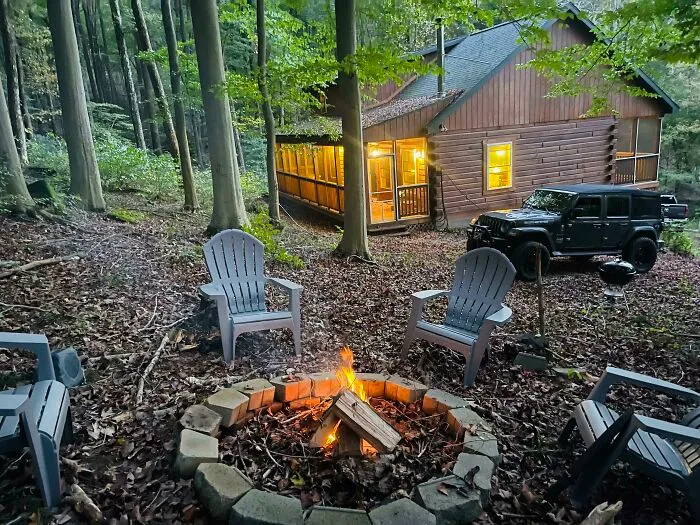 Cozy campfire scene with chairs around fire pit near a lit cabin and parked Jeep, inspiring big and small dreams realized.