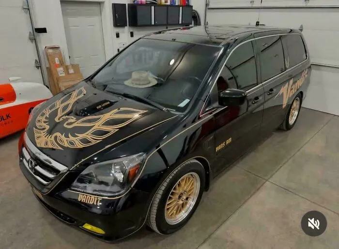 Black minivan customized with gold Pontiac Firebird decal and gold wheels, an example of people trying to make cars cooler.
