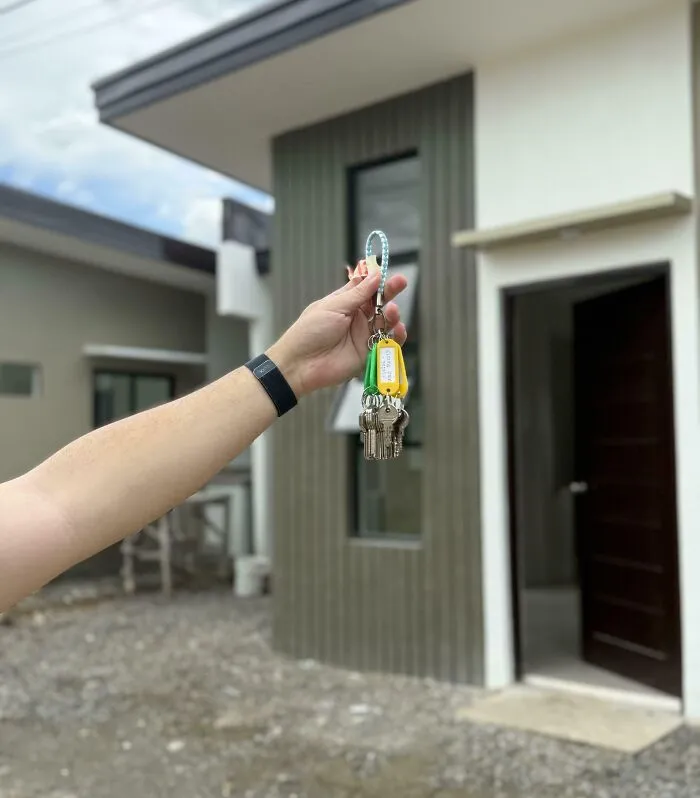Hand holding house keys in front of new home, symbolizing dreams turned into reality and inspiring achievement on the internet.