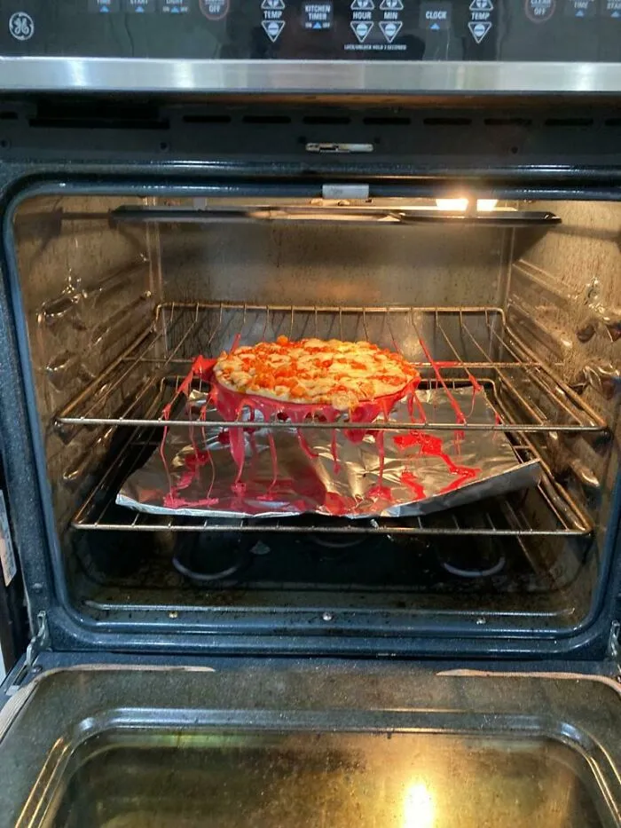 Pizza melting over the oven rack with red sauce dripping, showing a humorous men never grow up moment.