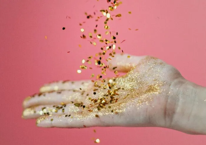 Mano con brillantina dorada cayendo sobre fondo rosa, simbolizando acciones de venganza contra ex parejas.