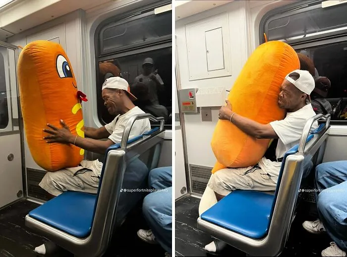Man on subway smiling and hugging a large plush hotdog, capturing wholesome internet moments online.