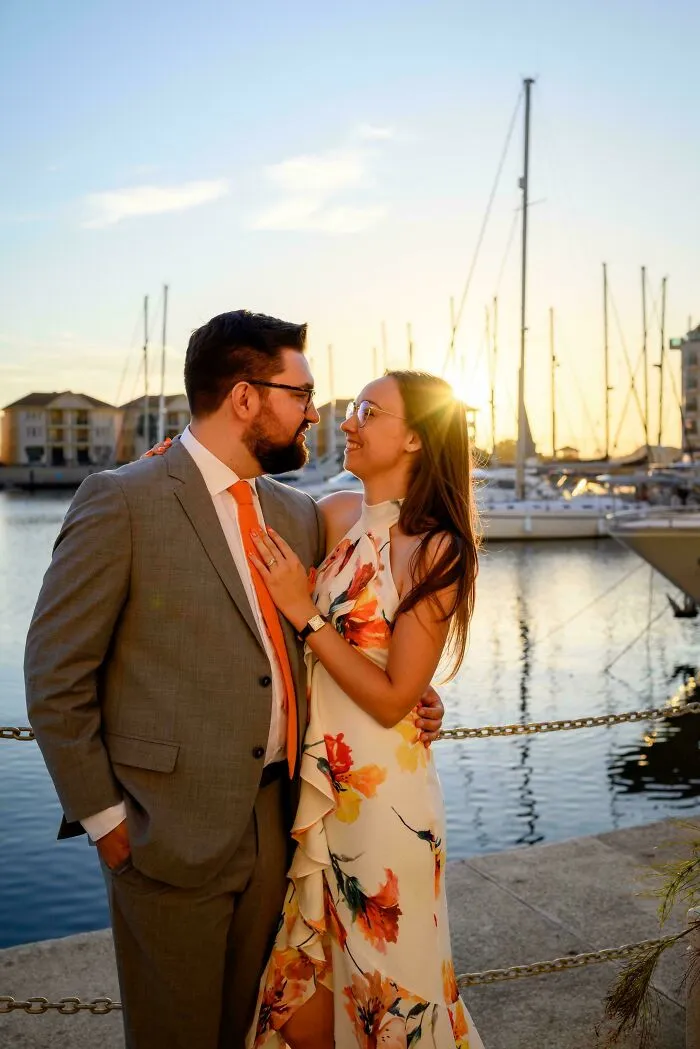 Couple smiling warmly at each other by the marina during sunset, representing wholesome internet moments.