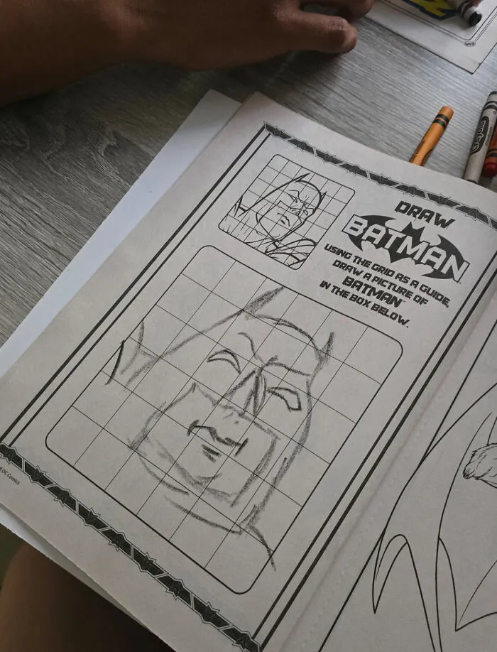 Hand drawing a Batman sketch using a grid guide, illustrating wholesome photos proving men never grow up.