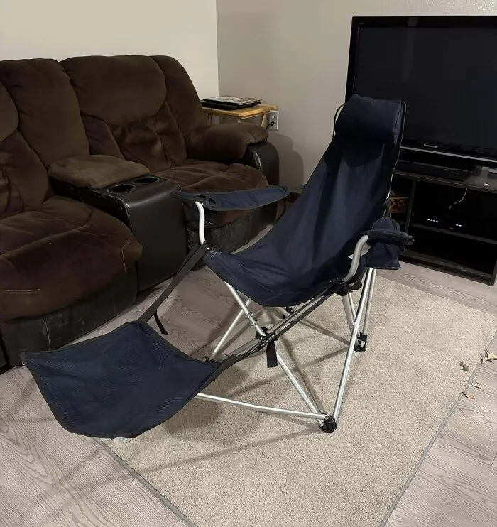 Collapsible reclining chair with footrest set up indoors near a brown couch and television, showcasing redneck engineer creativity.