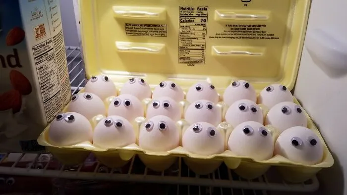 Egg carton with eggs inside a refrigerator, each egg decorated with googly eyes showing playful men never grow up humor.