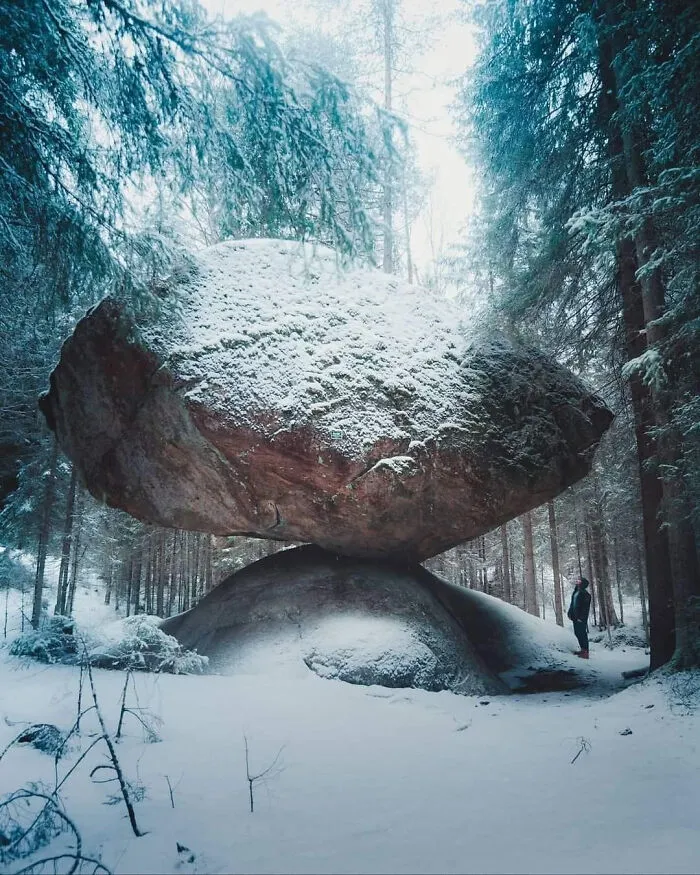 Huge snow-covered rock balanced in a winter forest, illustrating concepts of existence and reality in the universe.