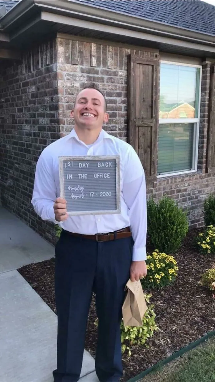 Smiling man holding a sign reading first day back in the office, capturing wholesome men never grow up moment outdoors.