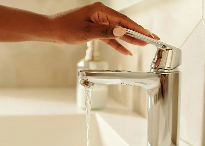 Hand turning on modern faucet with running water in a clean bathroom, illustrating lazy genius cleaning hacks.